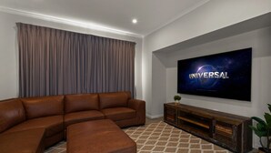 Un salon moderne avec un canapé d’angle, un téléviseur à écran plat fixé au mur et une console en bois.
