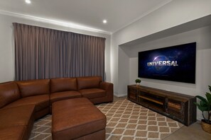 Un salon moderne avec un canapé d’angle, un téléviseur à écran plat fixé au mur et une console en bois.