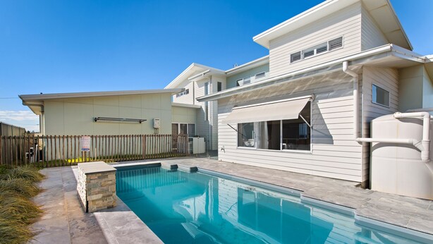 Una propiedad residencial con piscina, patio trasero cercado y una casa de dos plantas.
