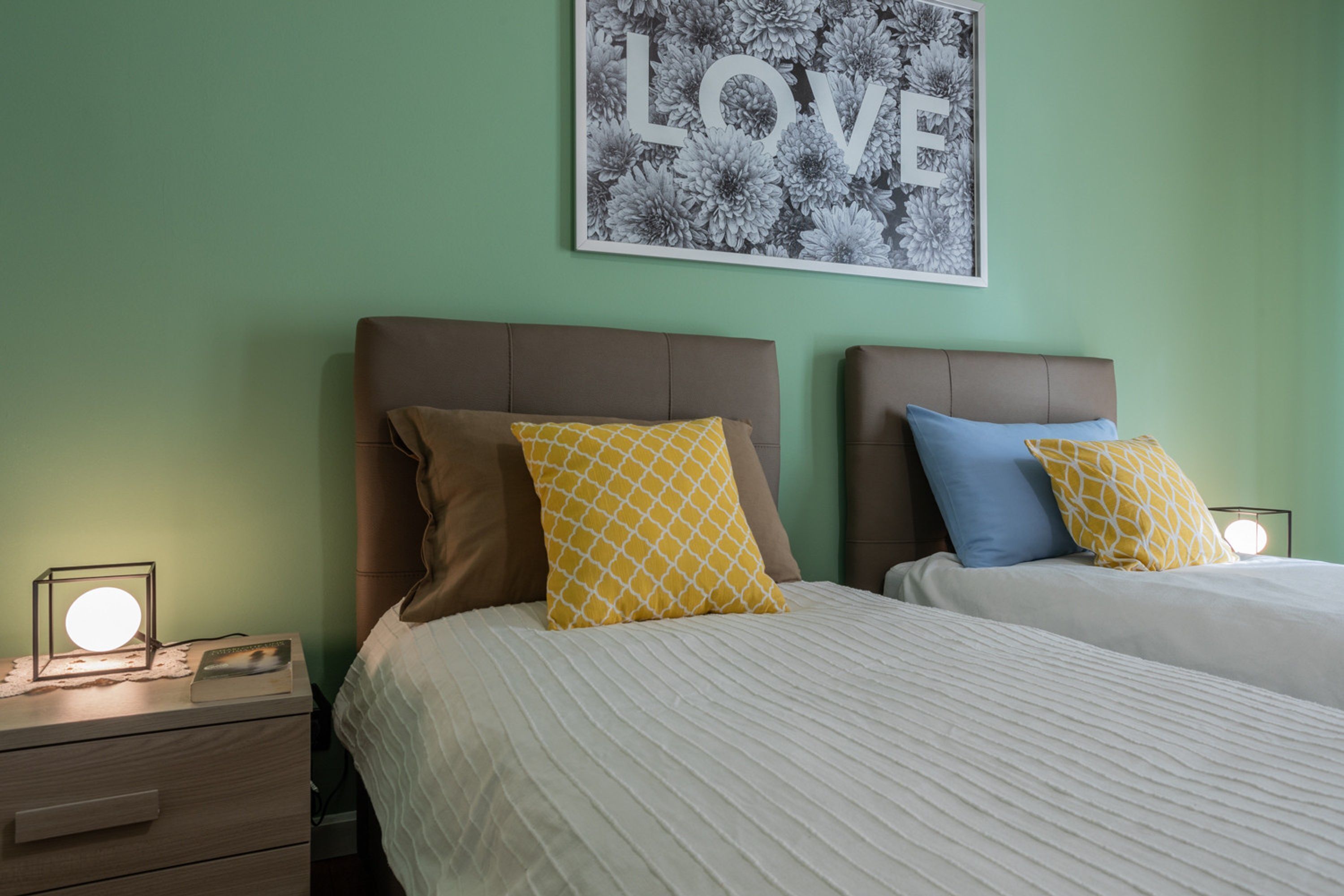 A bedroom with two beds, a nightstand with a lamp, and a wall art piece.