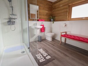 Un baño moderno con ducha envuelta en vidrio, un lavabo blanco, inodoro y un banco acolchado rojo.
