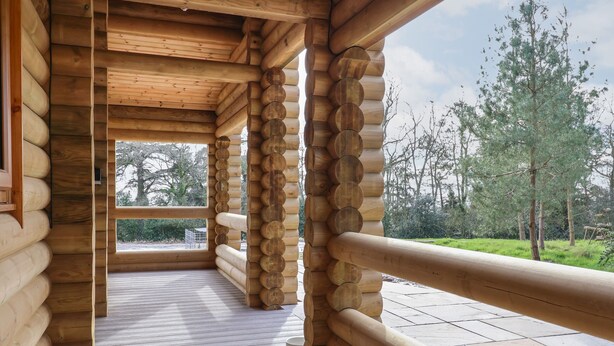 Interior de una cabaña de madera con una terraza de madera que conduce a una puerta de vidrio.