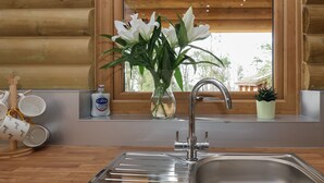 Una cocina con un lavamanos de acero inoxidable, una ventana con vistas a la vegetación y un jarrón con flores blancas.