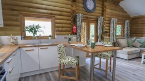 Interior de una cabaña de troncos con una mesa de comedor de madera, sillas, una zona de cocina y un sofá.