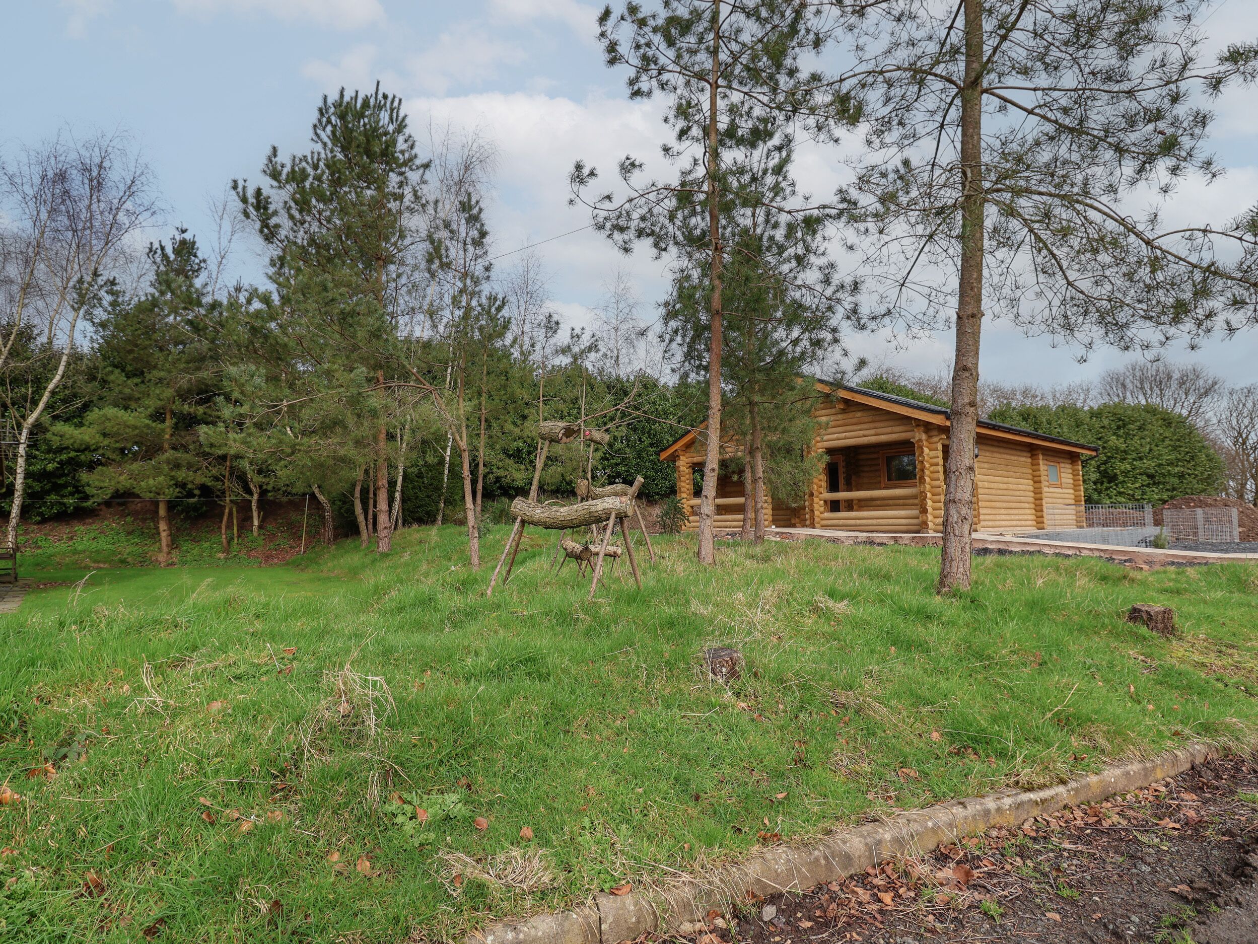 A rustic log cabin with a porch, surrounded by a grassy area and trees.