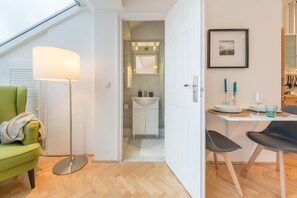 A modern kitchen with a white countertop, a dining area with two chairs, and a visible bathroom with a sink and mirror.