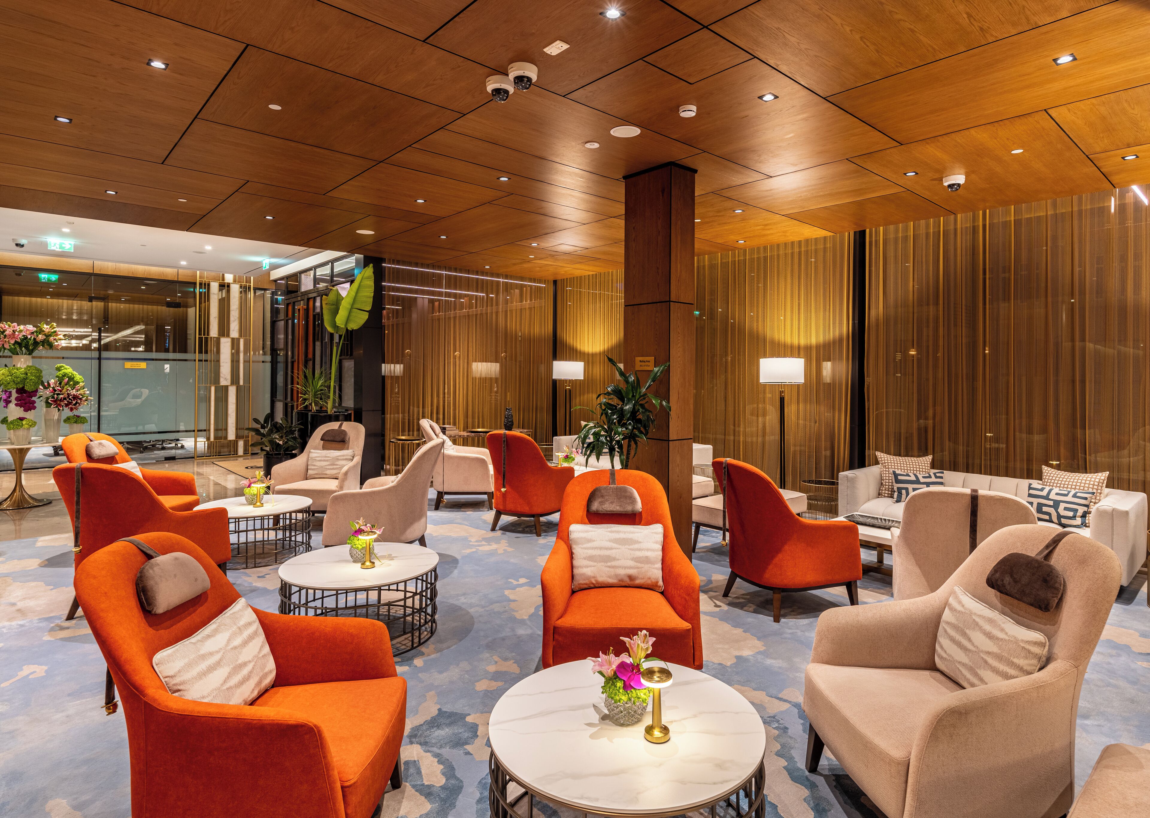 Un hall d’entrée doté de plusieurs espaces de détente, comprenant des fauteuils orange et beige, des tables rondes et une grande colonne.
