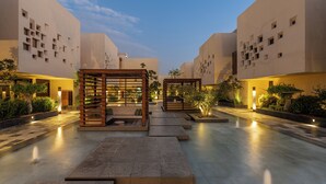 A modern hotel courtyard with geometric architecture, outdoor seating areas, and ambient lighting.
