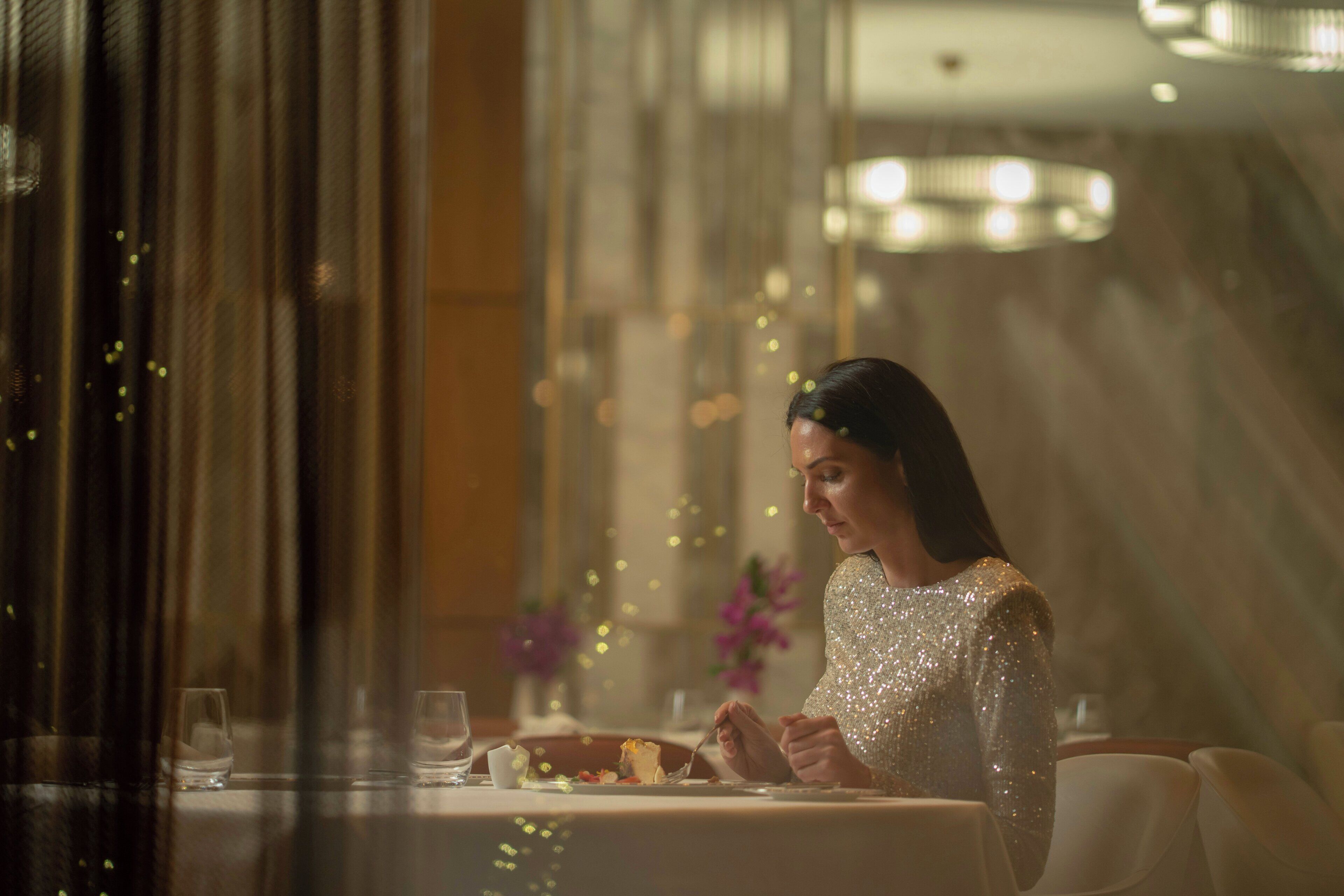 Une personne est assise à une table, devant un verre d’eau et une assiette de nourriture.