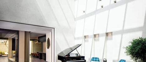 A spacious lobby with a grand piano, modern seating, and a large window allowing natural light.