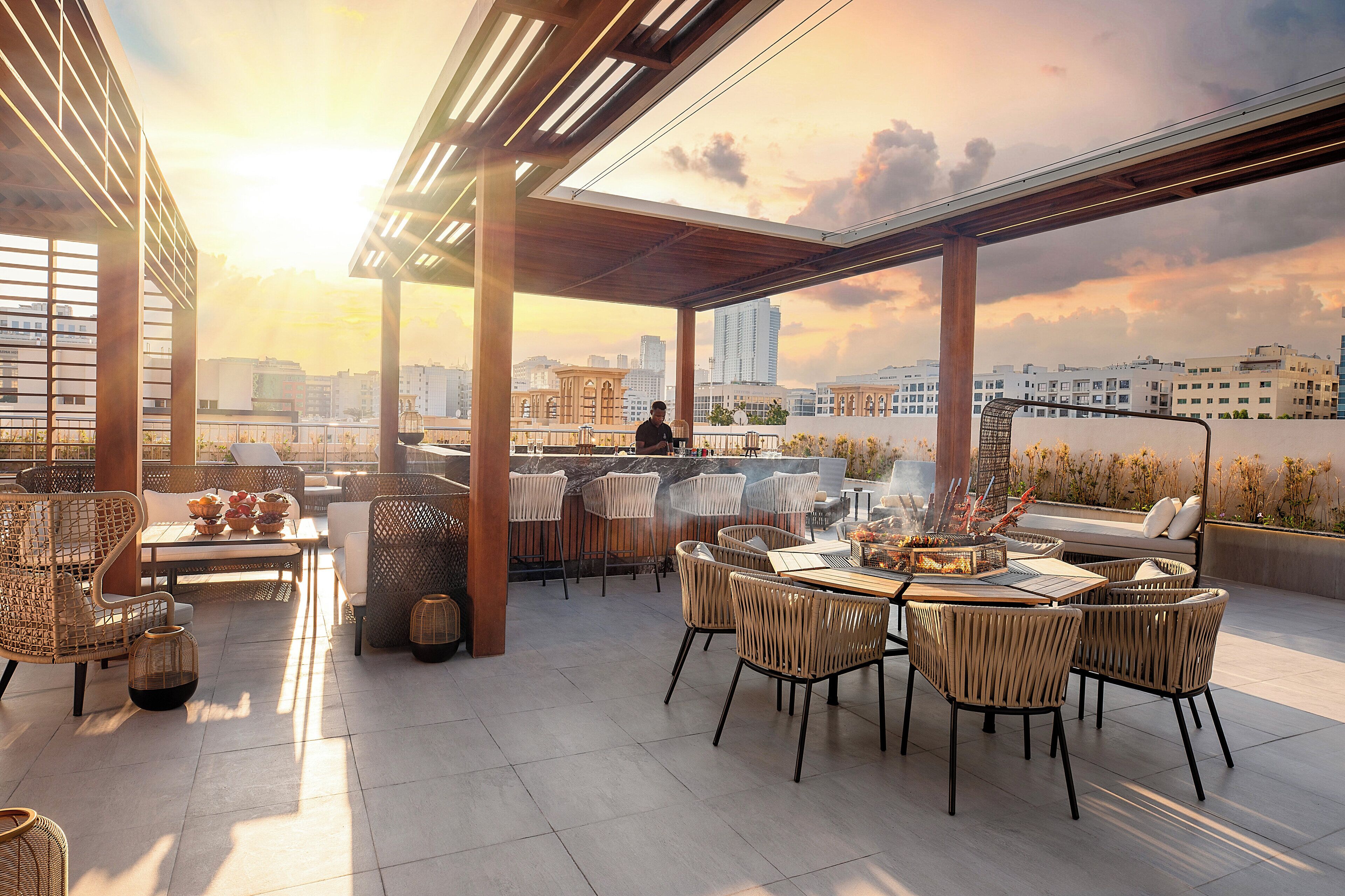 Un bar sul tetto con mobili in vimini, una griglia e vista sullo skyline della città.