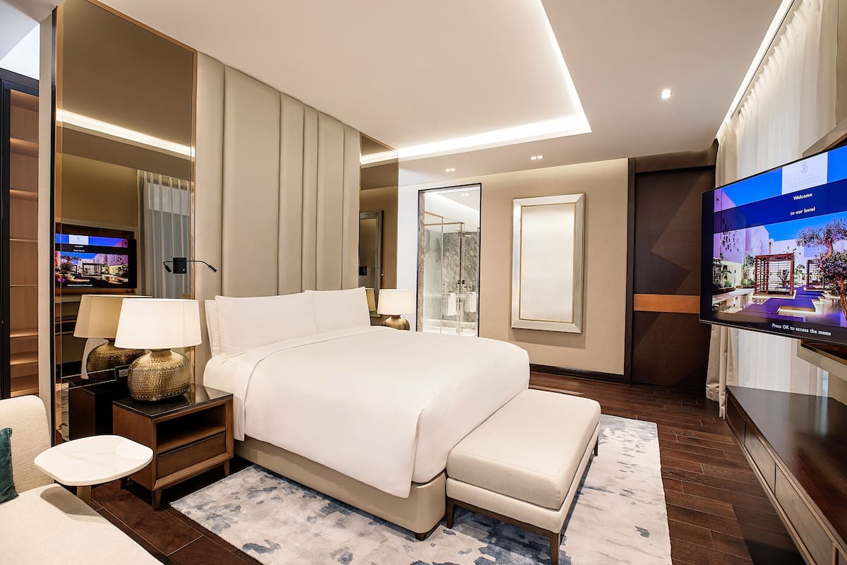 Ein modernes Hotelzimmer mit einem großen Bett, einem Fernseher, einem Nachttisch mit Lampe und einer kleinen Sitzecke.