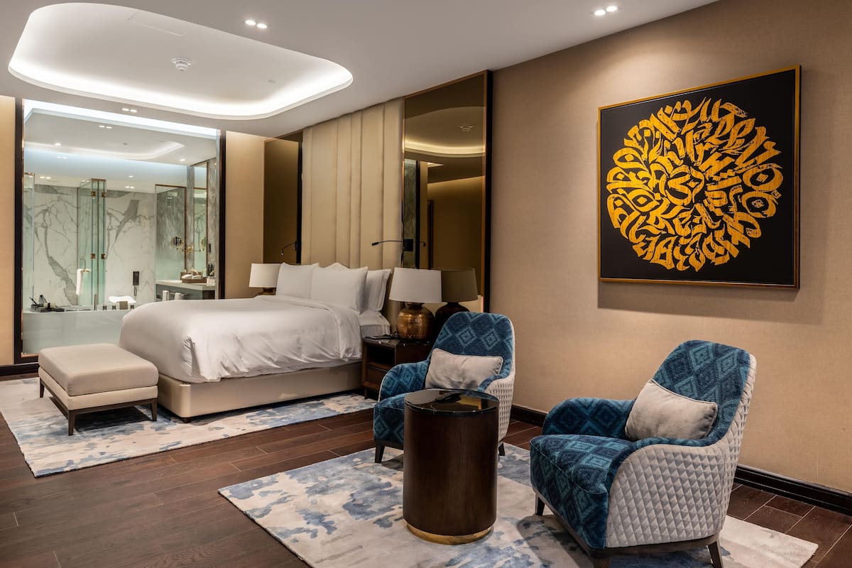 Ein modernes Hotelzimmer mit einem großen Bett, zwei Sesseln, einem kleinen Tisch und einem großen Kunstwerk an der Wand.