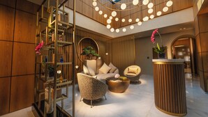 A modern lobby with a high ceiling, a central seating area with a round coffee table, and a wooden reception desk.