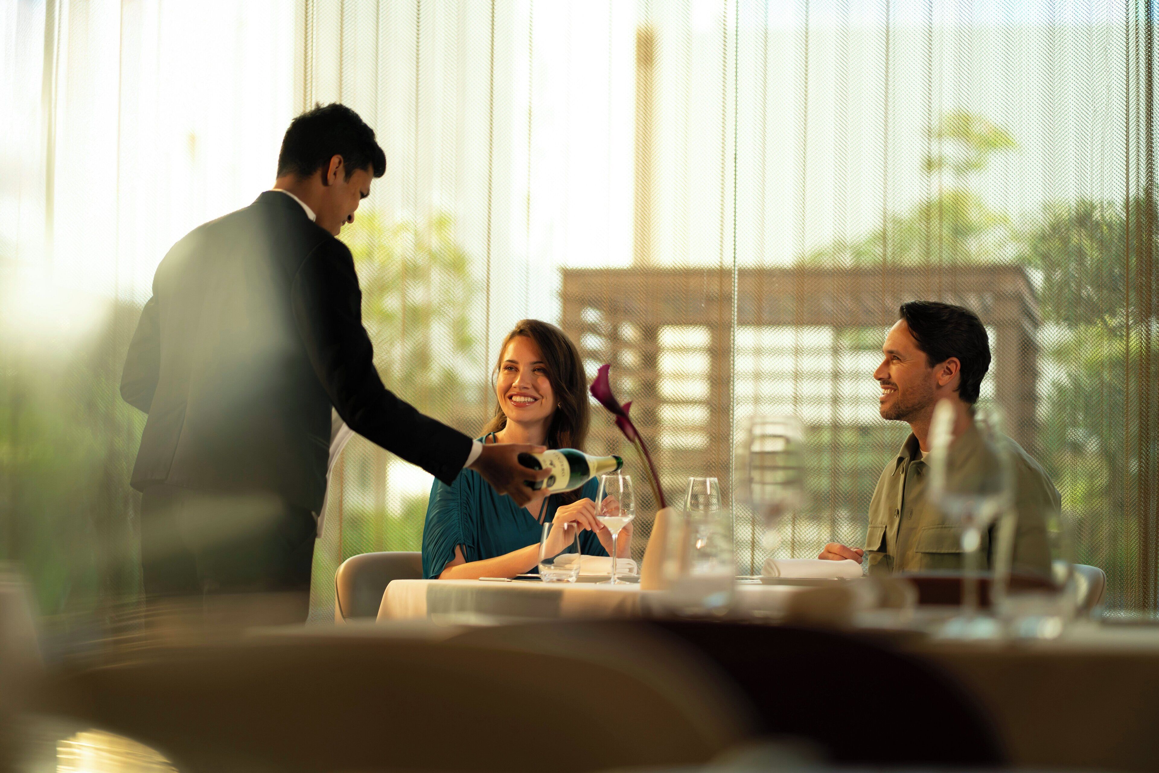 A dining table with a person pouring a drink into a glass.