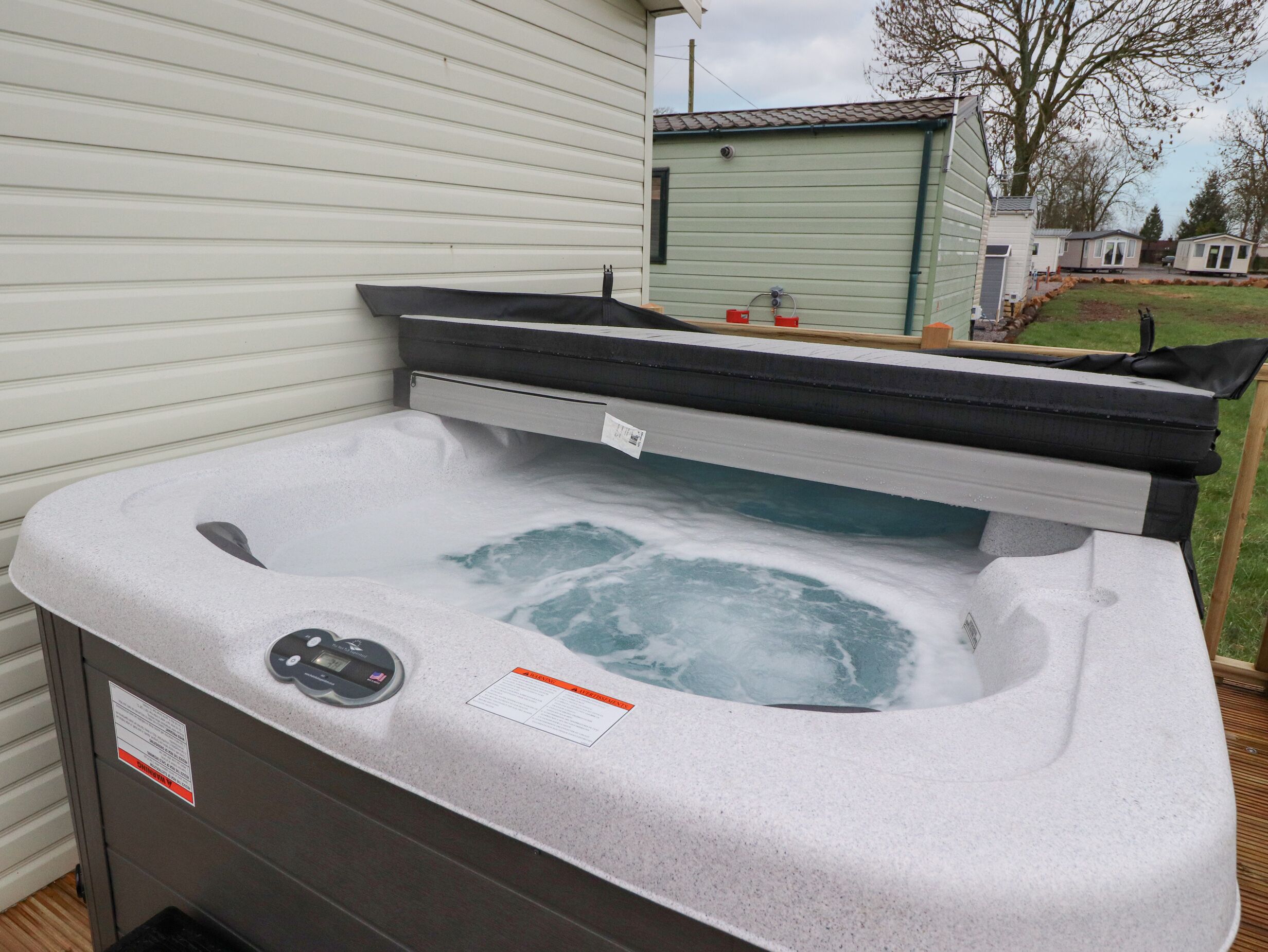 A hot tub with a control panel and a safety label, positioned outdoors near a house.