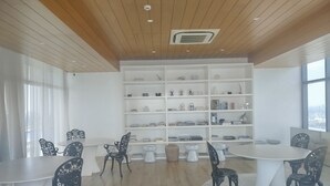 Un interior moderno con una mesa redonda, sillas negras, una estantería blanca y vistas a la ciudad a través de amplios ventanales.
