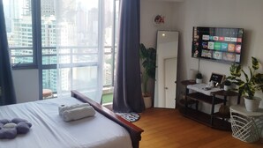 Habitación de hotel con cama, escritorio, televisor y vista a la ciudad.