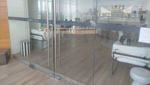 Un interior moderno con un separador de vidrio, piso de madera, sofá blanco y una zona de comedor con sillas y una mesa.