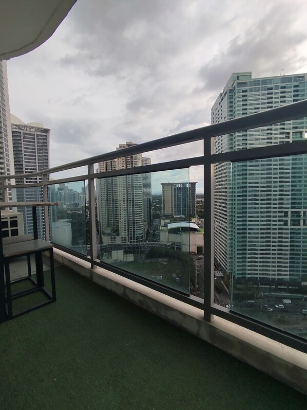 A balcony with a view of high-rise buildings, a glass railing, and a small table.