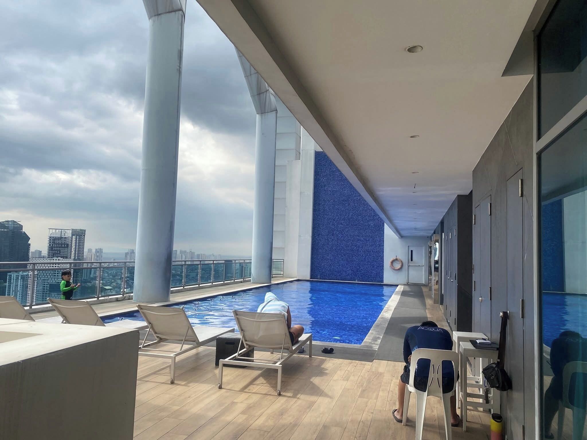 A rooftop pool area with lounge chairs, a pool, and a city view.