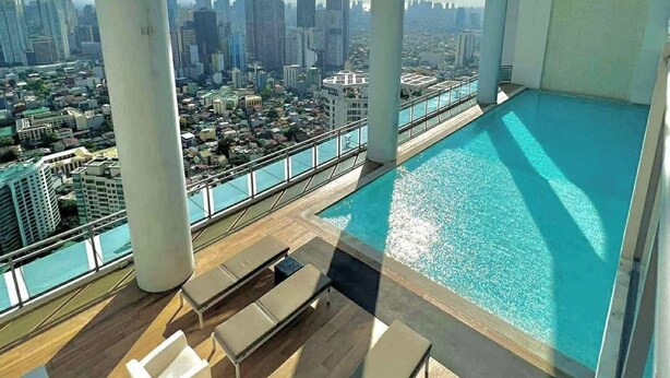 Piscina en la azotea con vistas a la ciudad, sillas de descanso y zona acristalada.
