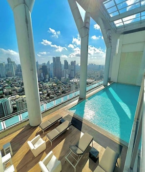 A rooftop pool with a city view, lounge chairs, and a glass-enclosed area.