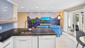 Eine moderne Küche mit eingebautem Geschirrspüler, einem blauen Sofa und einem großen Fernsehbildschirm.