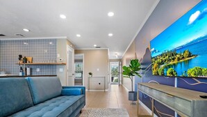 Ein modernes Wohnzimmer mit einem blauen Sofa, einem an der Wand montierten Fernseher und einem großen Fenster mit Blick auf eine malerische Landschaft.