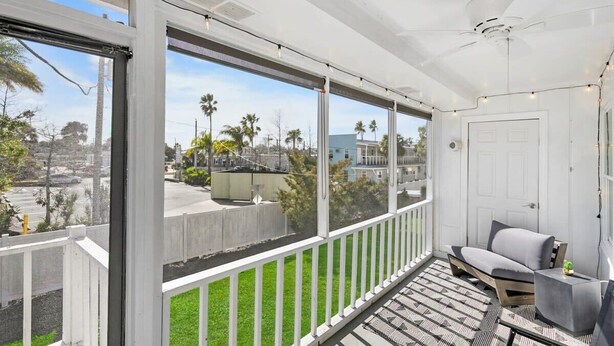 Ein Balkon mit Blick auf Palmen und Gebäude, einem Deckenventilator sowie einer Sitzecke mit einer Bank und einem kleinen Tisch.