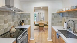 A modern kitchen with a stove, oven, and a kettle on the counter. There is a dining area with a table and chairs in the background. - Walk Downtown, Free Parking, By Conch House, Games (St. Augustine)