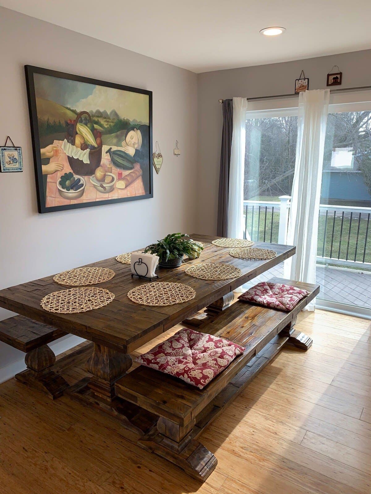 Una zona de menjador amb una taula de fusta llarga, sobreades teixides i bancs amb coixins.