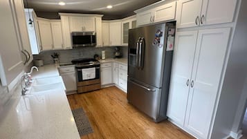A modern kitchen with white cabinetry, stainless steel appliances, and a wooden floor.