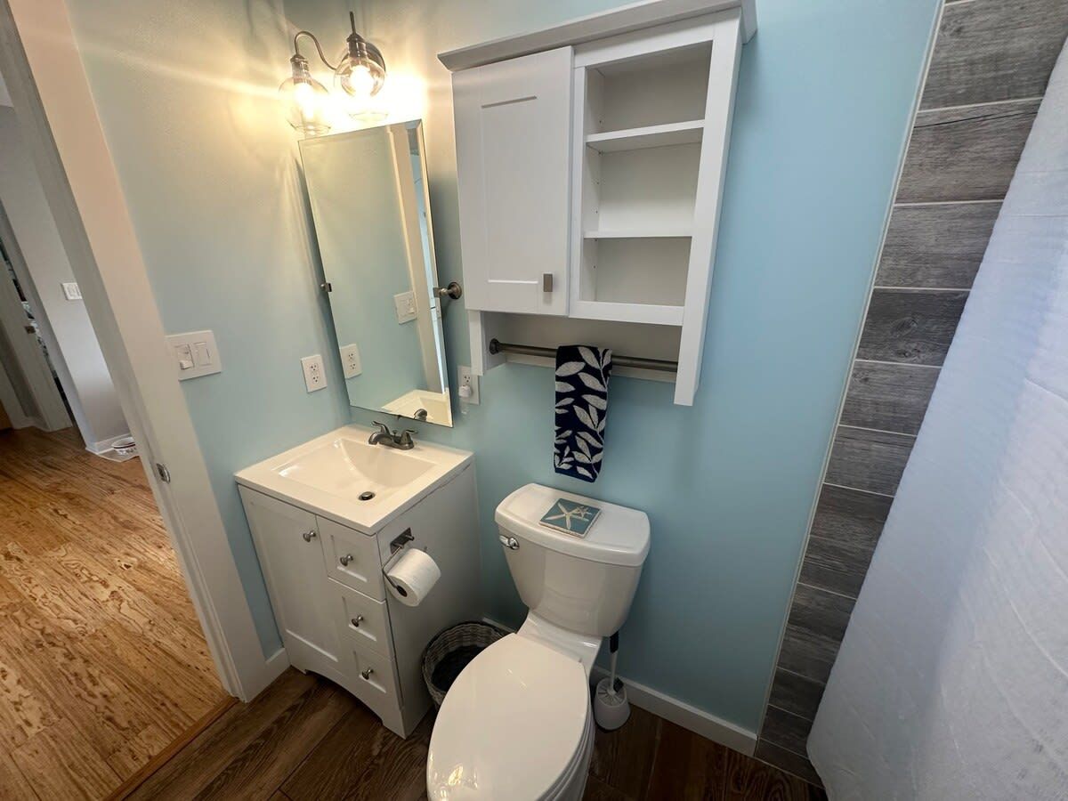 Un baño con lavamanos blanco, inodoro y un mueble sobre el inodoro.