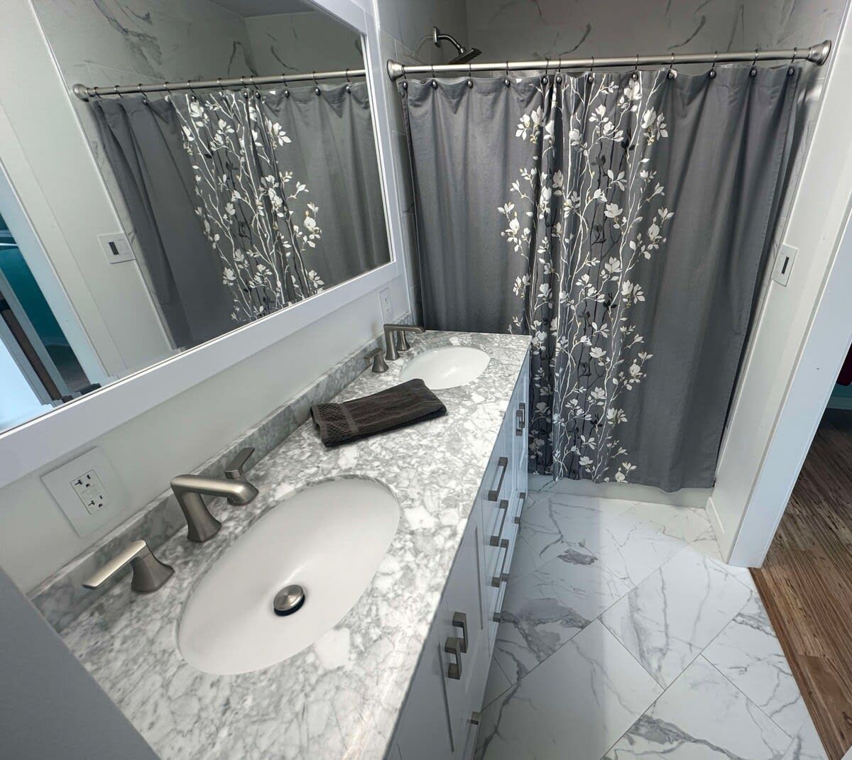 A bathroom with a marble sink, a mirror, a towel, and a shower curtain with a floral pattern.
