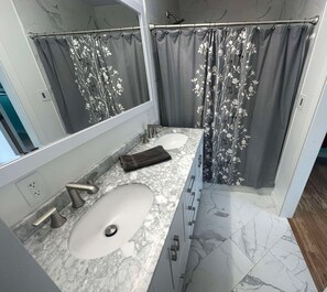 Un baño con lavamanos de mármol, un espejo, una toalla y una cortina de ducha estampada con motivos florales.