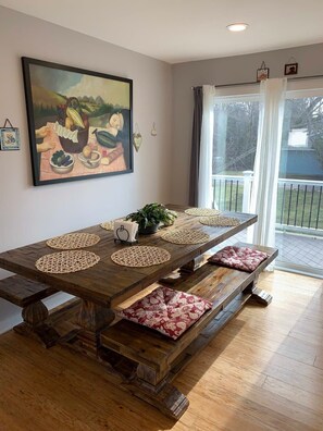 Une table à manger agrémentée de sets de table en fibres tressées, des bancs avec des coussins à motifs, un tableau accroché au mur et une vue sur l’extérieur grâce à une porte vitrée.