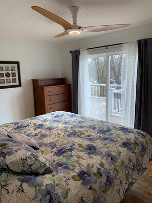 Un dormitorio con cama, ventilador de techo, cómoda y ventana con cortinas.