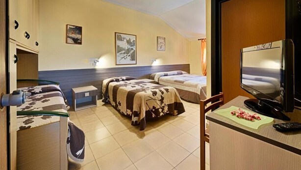A hotel room with two beds, a television, a desk with a computer, and a small table. - Albergo Mancuso del Voison (Aosta)