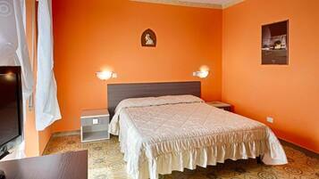 Una camera da letto con una parete arancione, un letto con copriletto beige, due lampade da comodino, un comodino piccolo, una TV e un pavimento a motivi.