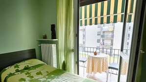 A bedroom with a bed, a radiator, a window with curtains, and a balcony with a table and chairs. - Albergo Mancuso del Voison (Aosta)