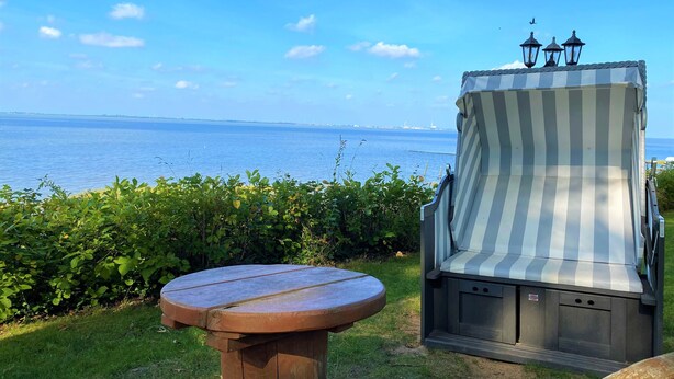 Eine Strandlounge mit Blick aufs Meer, ein gestreifter Liegestuhl und ein kleiner Holztisch.