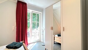 Een slaapkamer met een bed, een kledingkast, een raam met gordijnen en uitzicht op het buiten.