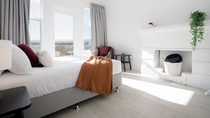 Un dormitorio moderno con cama, una mesita, una silla, chimenea y vistas a la ciudad.