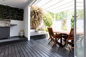Une terrasse extérieure avec un barbecue, une table en bois et des chaises.