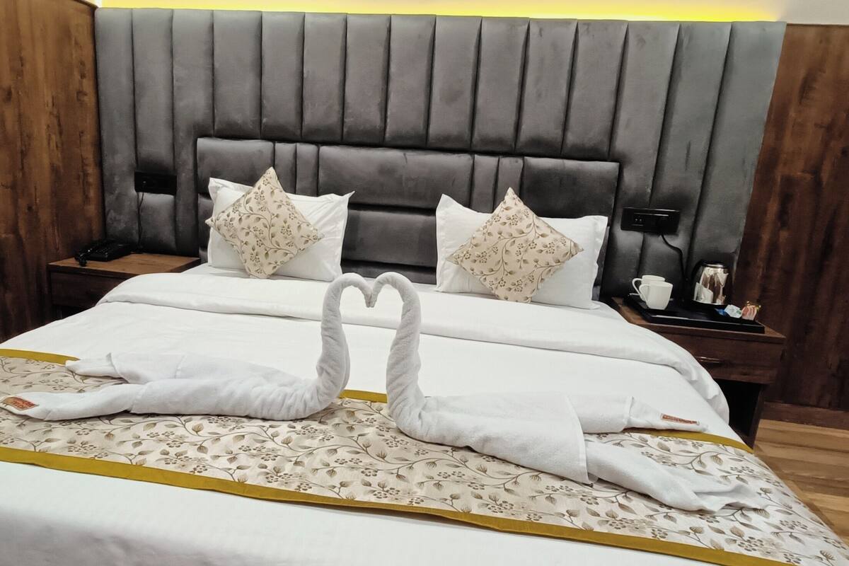 Una cama bien hecha con dos toallas con forma de cisne, una colcha estampada con motivos florales y un cabecero con diseño de panel vertical.