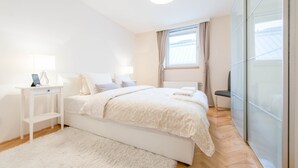 A bedroom with a bed, bedside tables, a desk, a chair, and a large window with curtains.