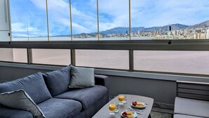 Une chambre moderne dotée d’une grande fenêtre donnant sur un paysage urbain et sur une étendue d’eau.