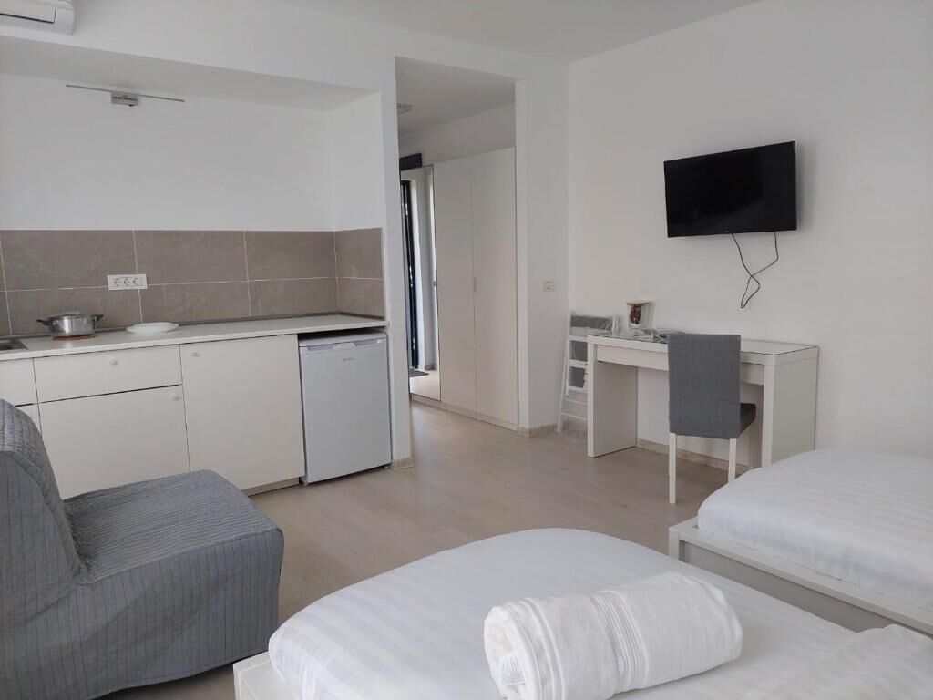 Habitación de hotel moderna con kitchenette, televisor de pantalla plana, escritorio y dos camas.
