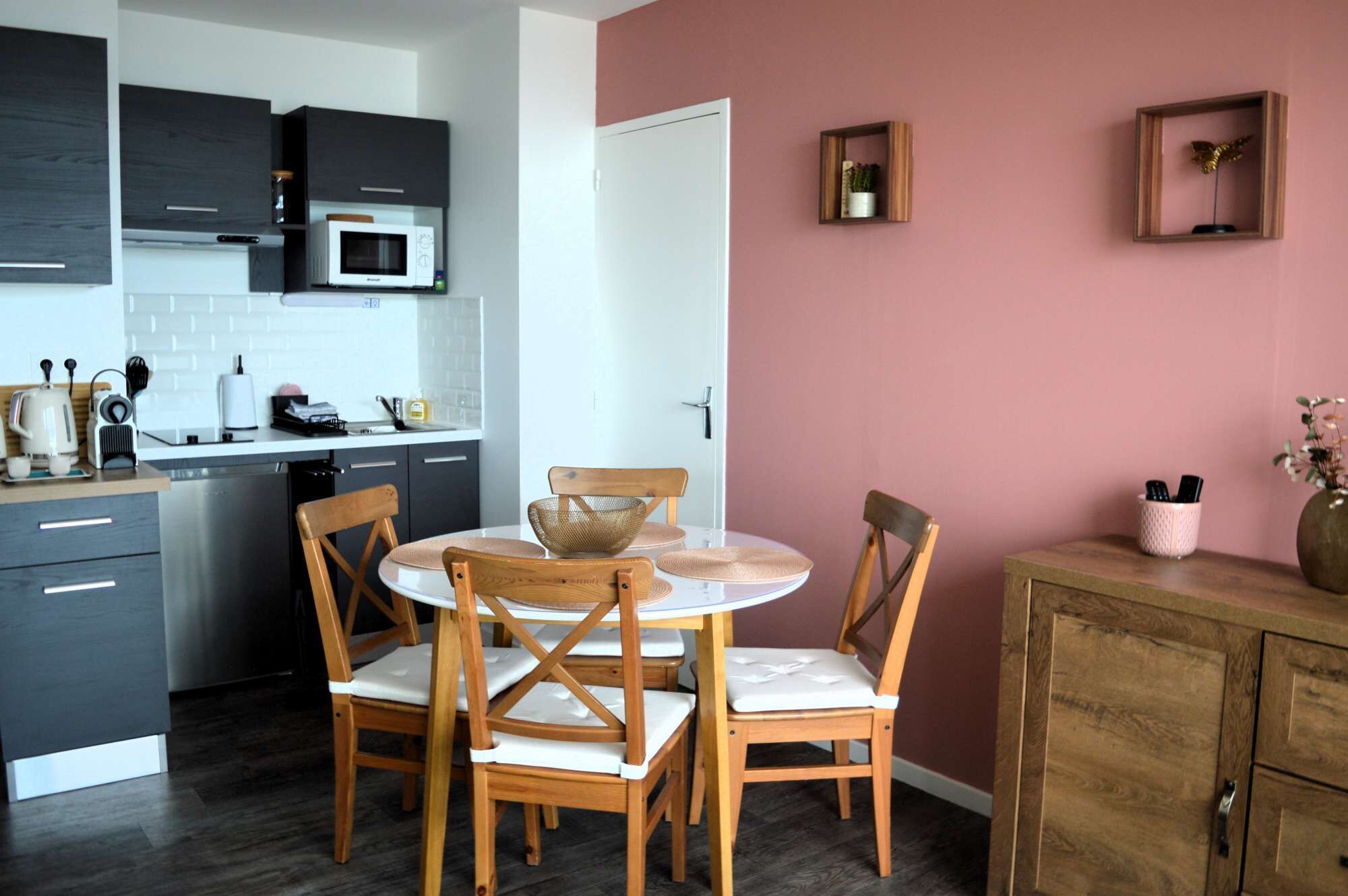 A modern kitchen with dark cabinets, a microwave, and a dining area with wooden chairs and a white table.